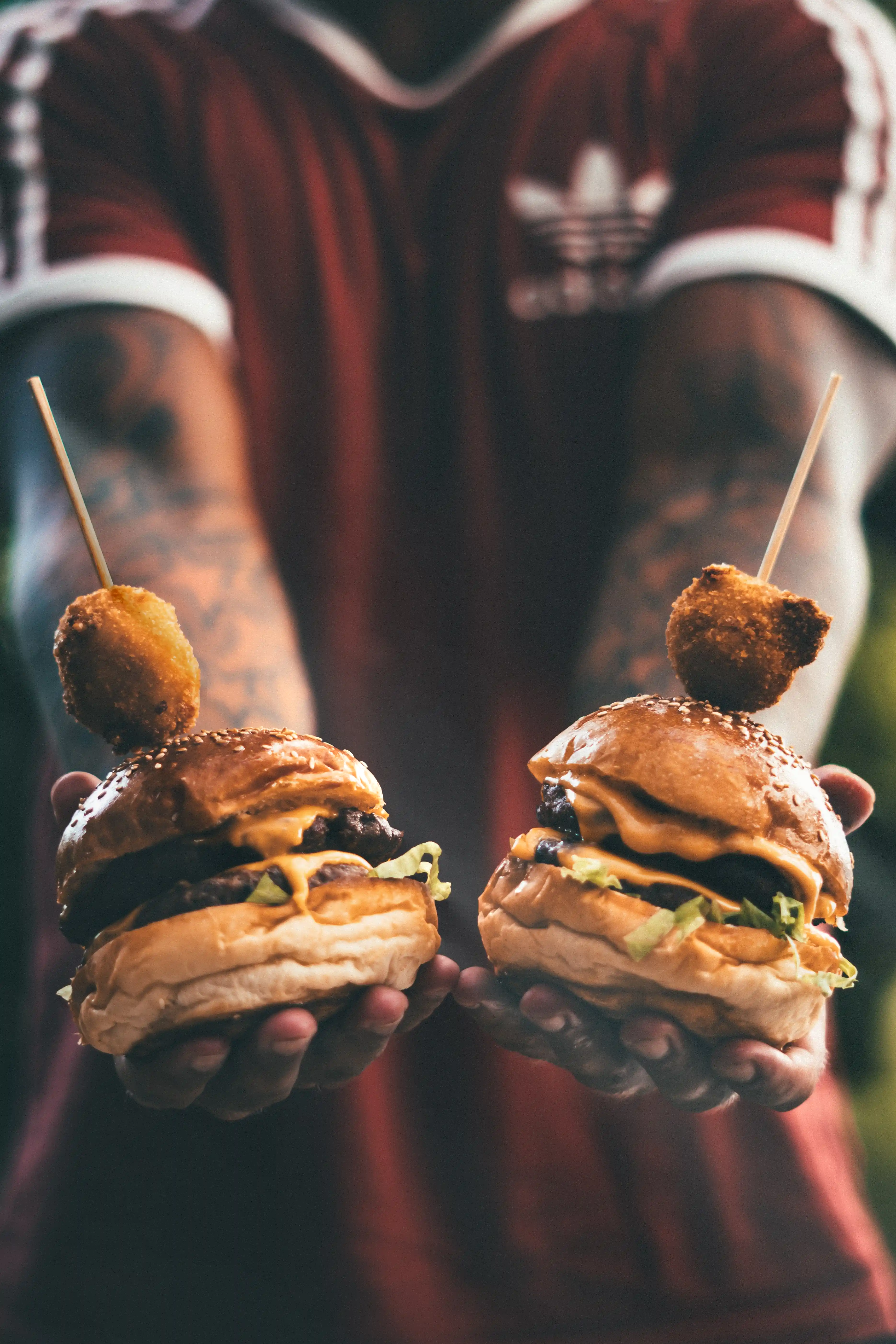 Guy holding 2 hamburgers with skewers in them